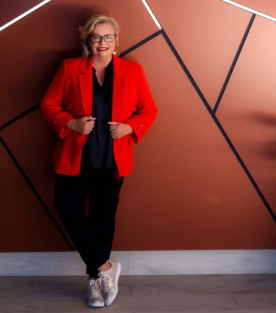 Picture of Sally Porteous, founder of Red Lanyard and event management and production professional, dressed in a red jacket leaning against a copper wall.